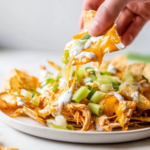 Hearty platter of baked Buffalo Chicken Nachos topped with ranch drizzle, diced celery, and tomatoes, ready for game day sharing.