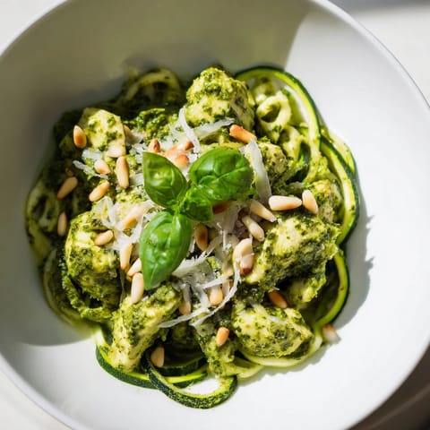 A close-up of tender chicken, spiralized zucchini, and fresh basil leaves in a light, summery pesto sauce.  