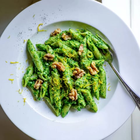 Creamy Spinach Walnut Pasta plated on a rustic wooden table, surrounded by fresh spinach leaves and whole walnuts for a fresh, farm-to-table feel.