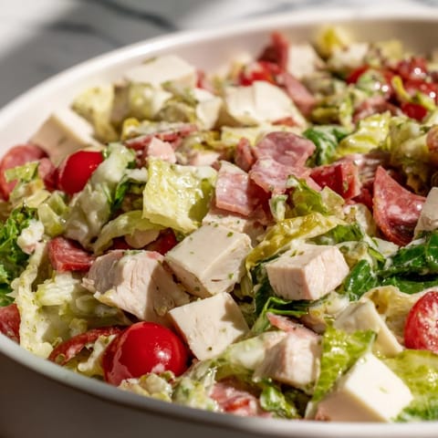 A vibrant Italian Deli Chopped Chicken Salad with crispy romaine, chopped chicken, salami, provolone, and pepperoncini on a rustic plate.