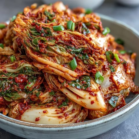 In a clear glass jar, freshly made kimchi rests with its spicy, tangy fermentation paste clinging to each vegetable piece.