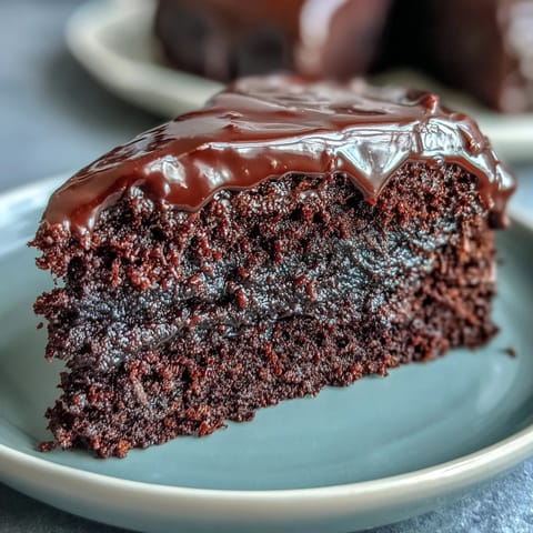 A close-up view of sliced Easy Chocolate Fudge Cake showing silky chocolate icing on top and a rich, fudgy texture inside.