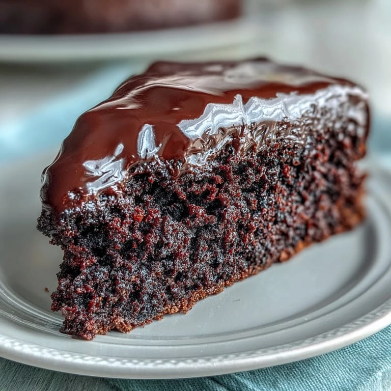 Easy Chocolate Fudge Cake decorated with chocolate shavings, sitting on a cooling rack beside a cup of black coffee.