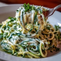 Creamy cottage cheese Alfredo sauce drizzled over tender zucchini noodles in a vibrant, healthy dish.  